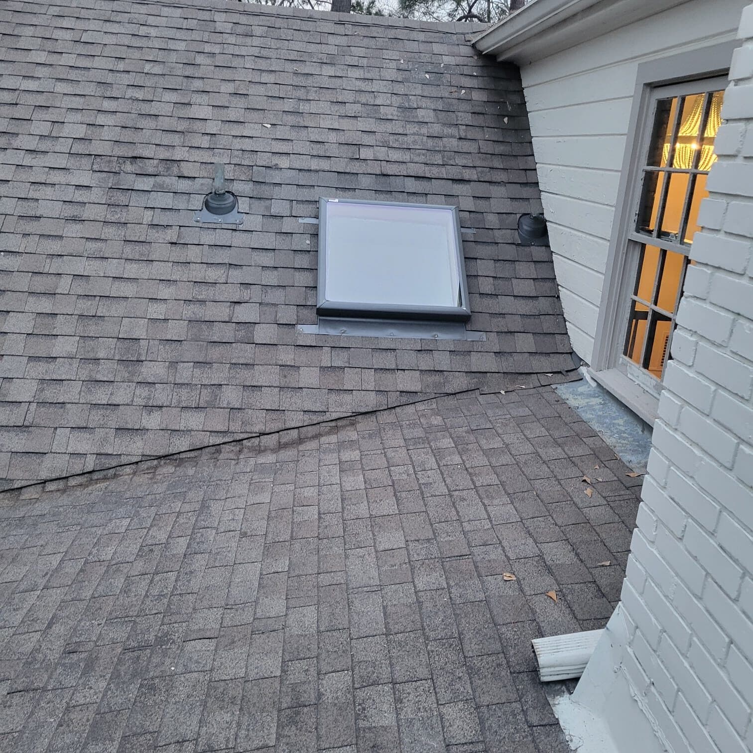 New architectural shingle roof with a vent beside a white painted brick wall and window