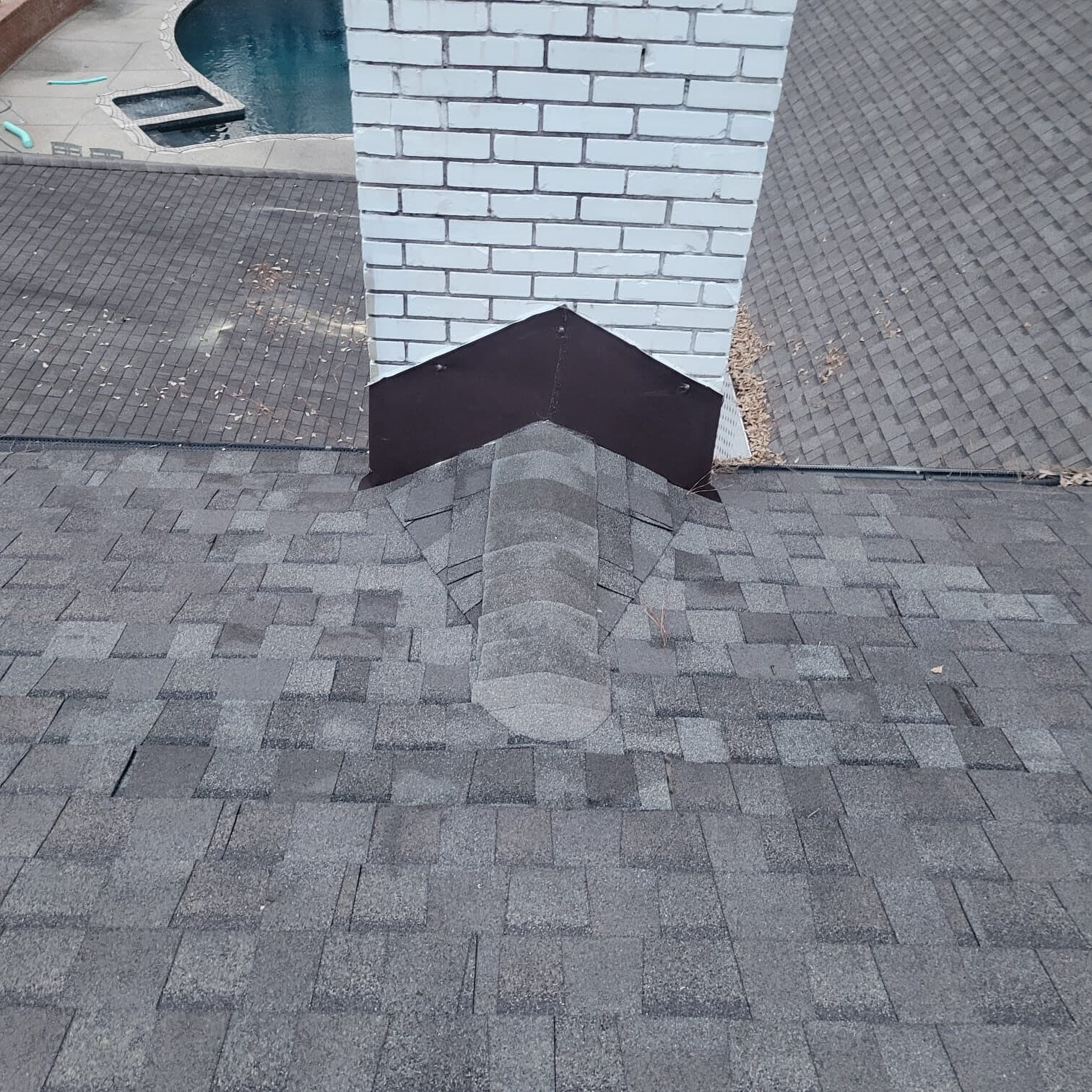 White brick chimney with a new metal cricket and step flashing on an architectural shingle roof