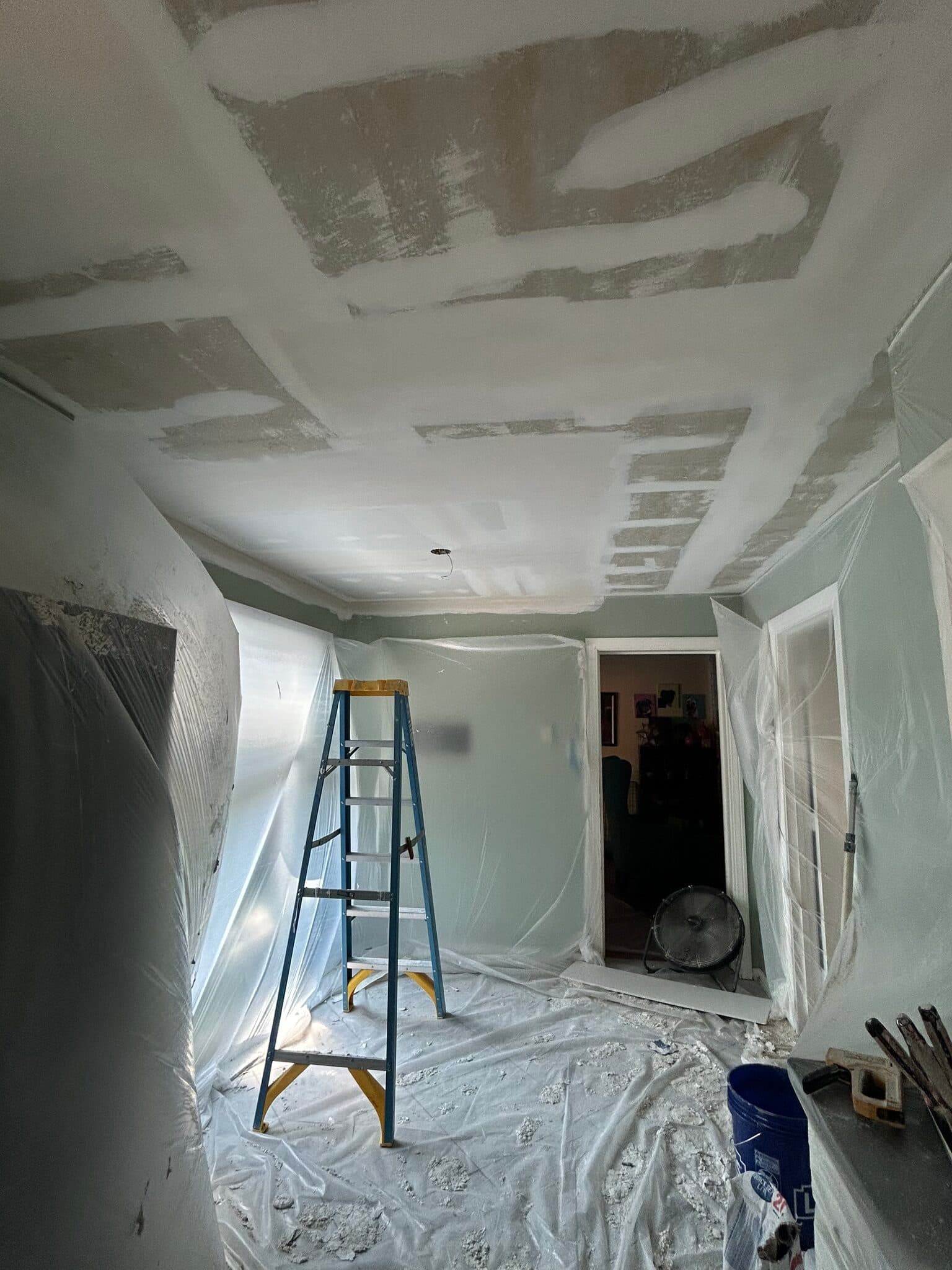 Room mid-drywall finish with taped ceiling joints, a step ladder, and plastic-sheeted walls