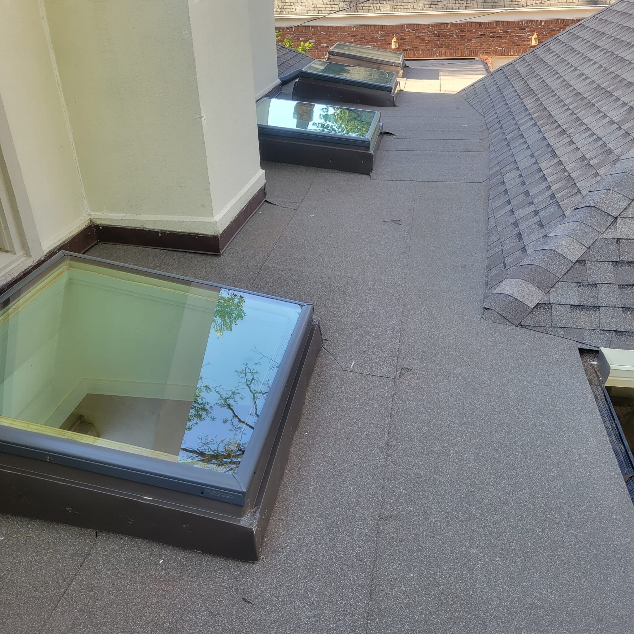 Skylight curb on a low-slope roof with a shingle ridge behind it