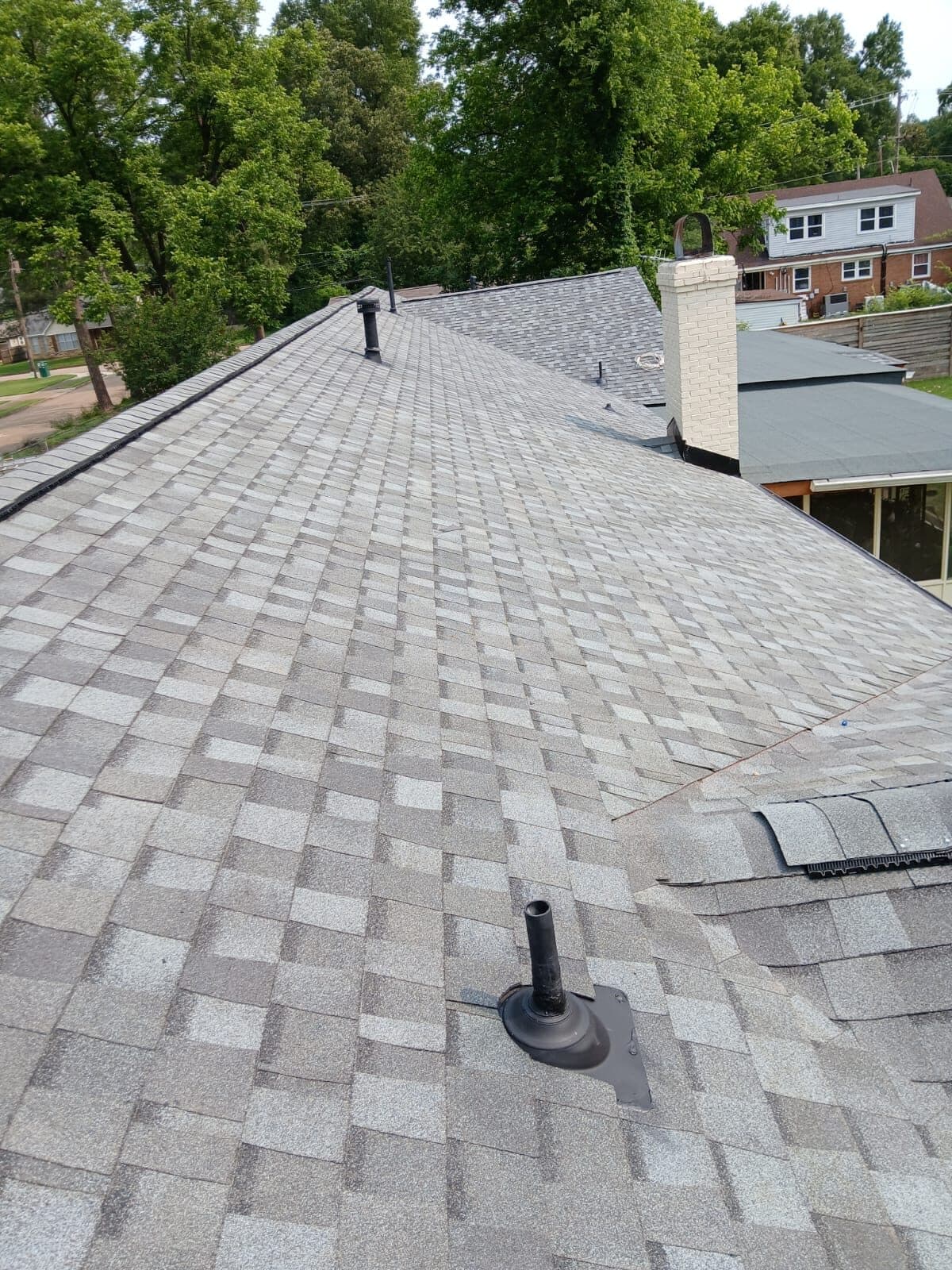 Wide field of light gray architectural shingles with a pipe boot and distant chimney