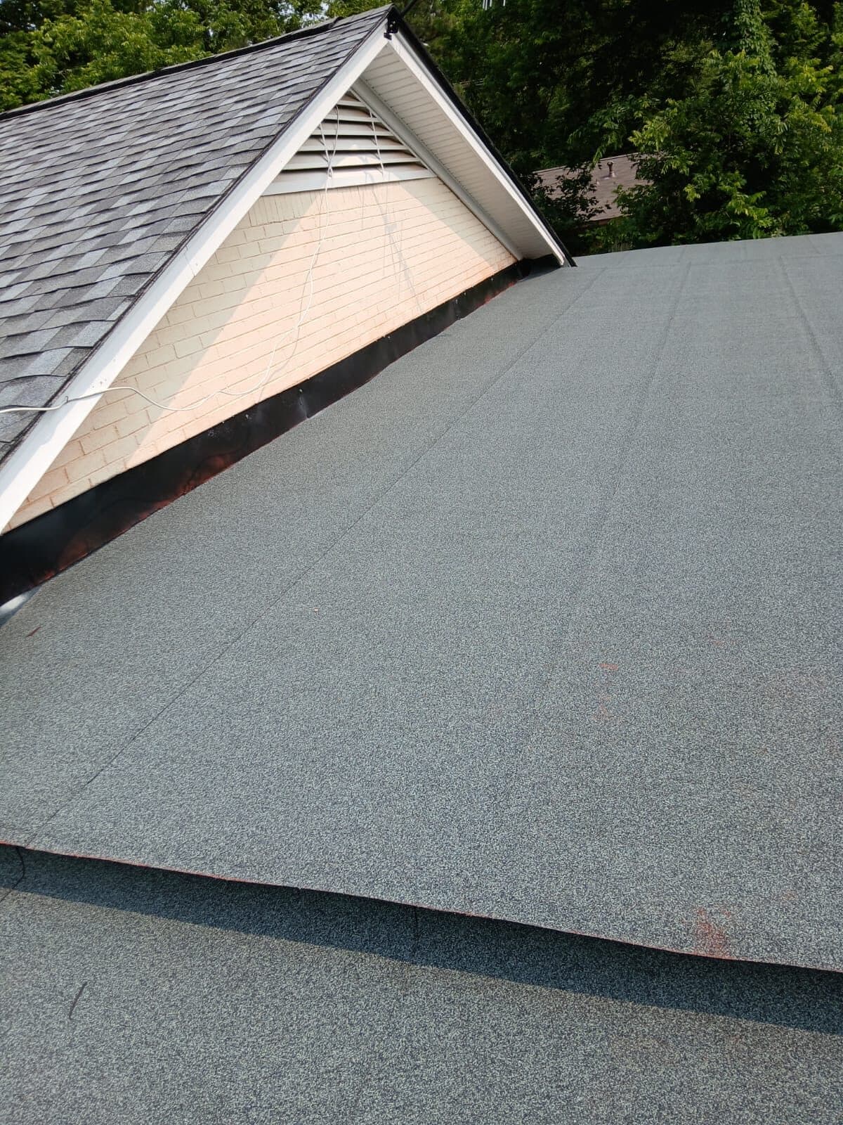 Gable end with ridge vent transitioning to a low-slope granulated roof section