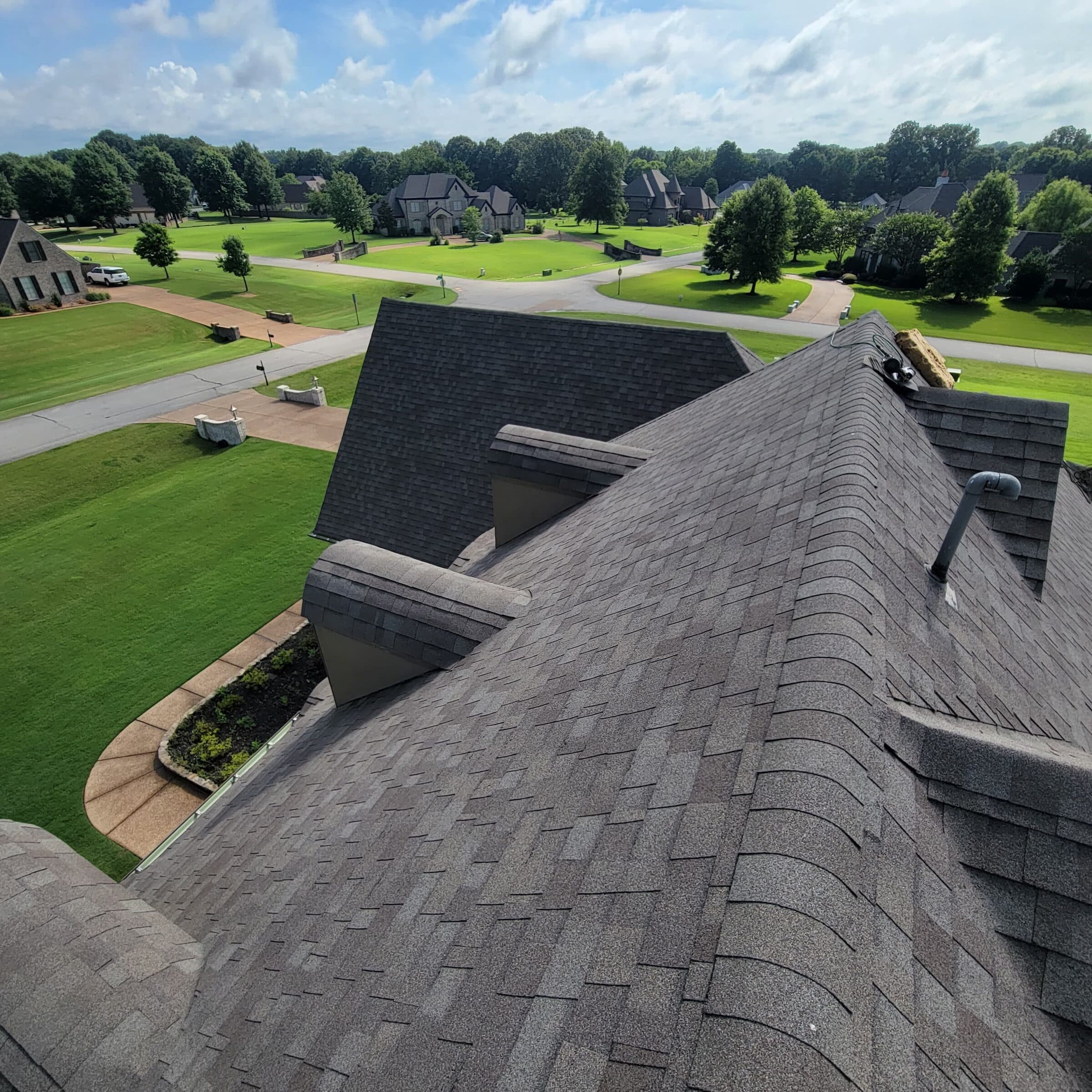 View from a rooftop ridge over a golf course community with new dark shingles in the foreground