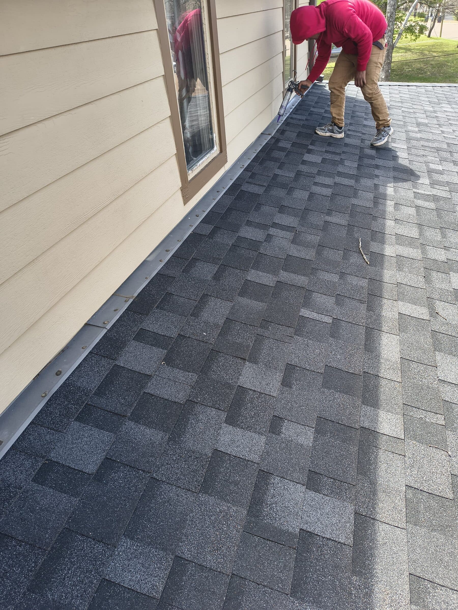 Crew member installing new shingles along a wall and roof junction
