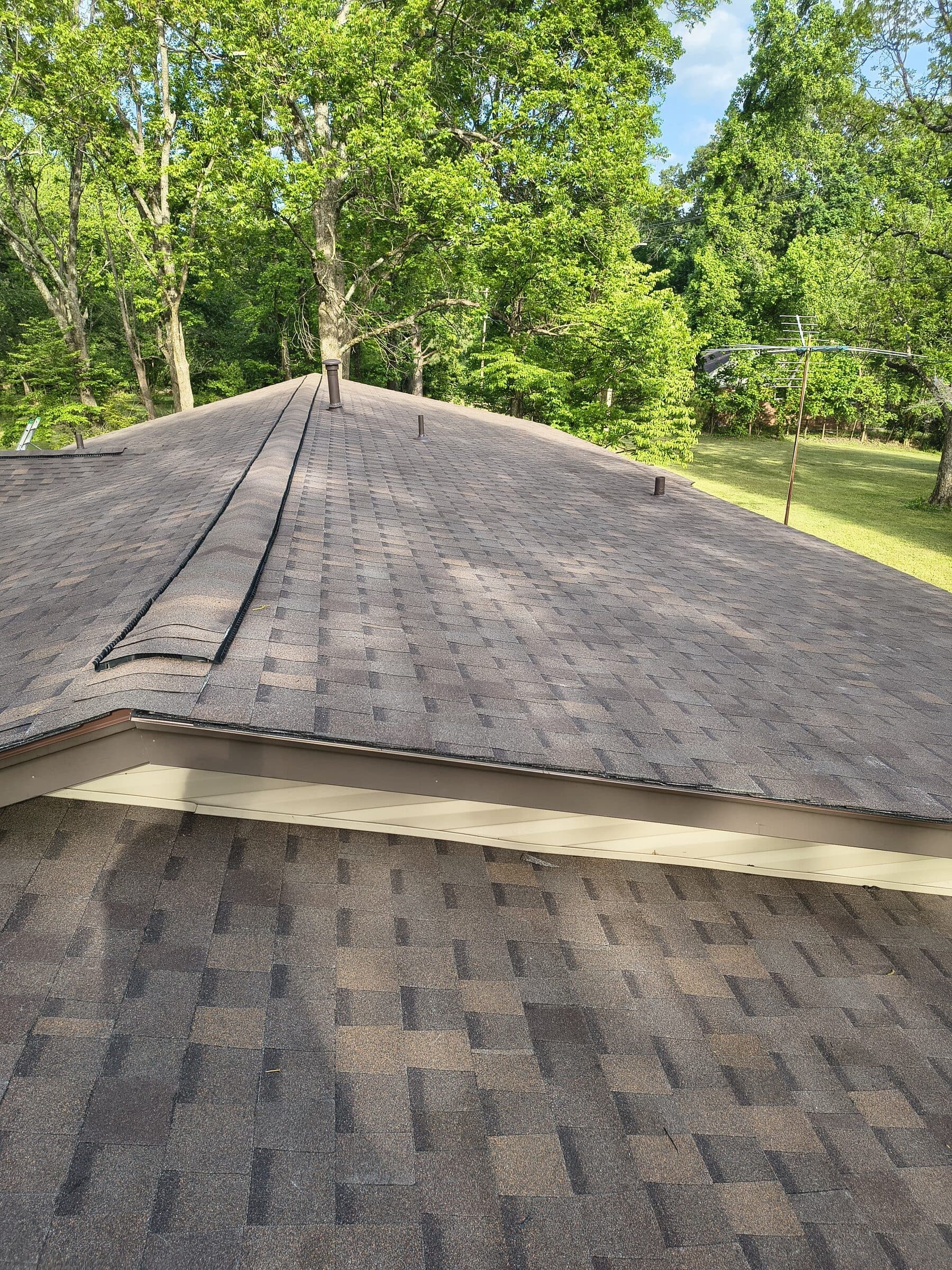 Hip roof peak with new dark shingles against a wooded backdrop