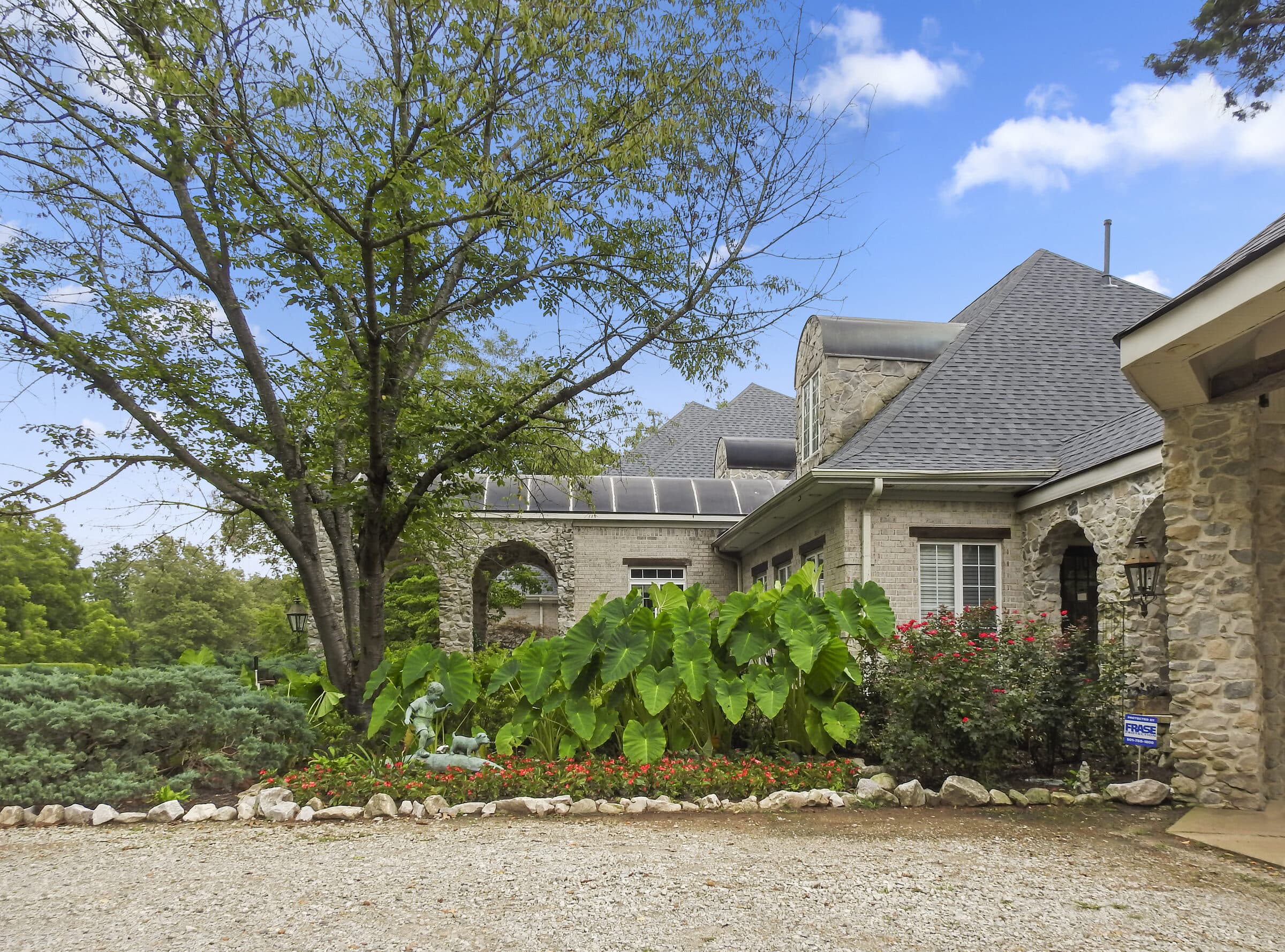 Brick and stone home with a mature shade tree and completed roof