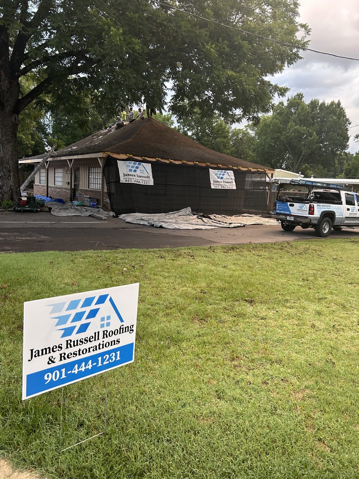 James Russell Roofing yard sign on a front lawn with a crew truck at the curb