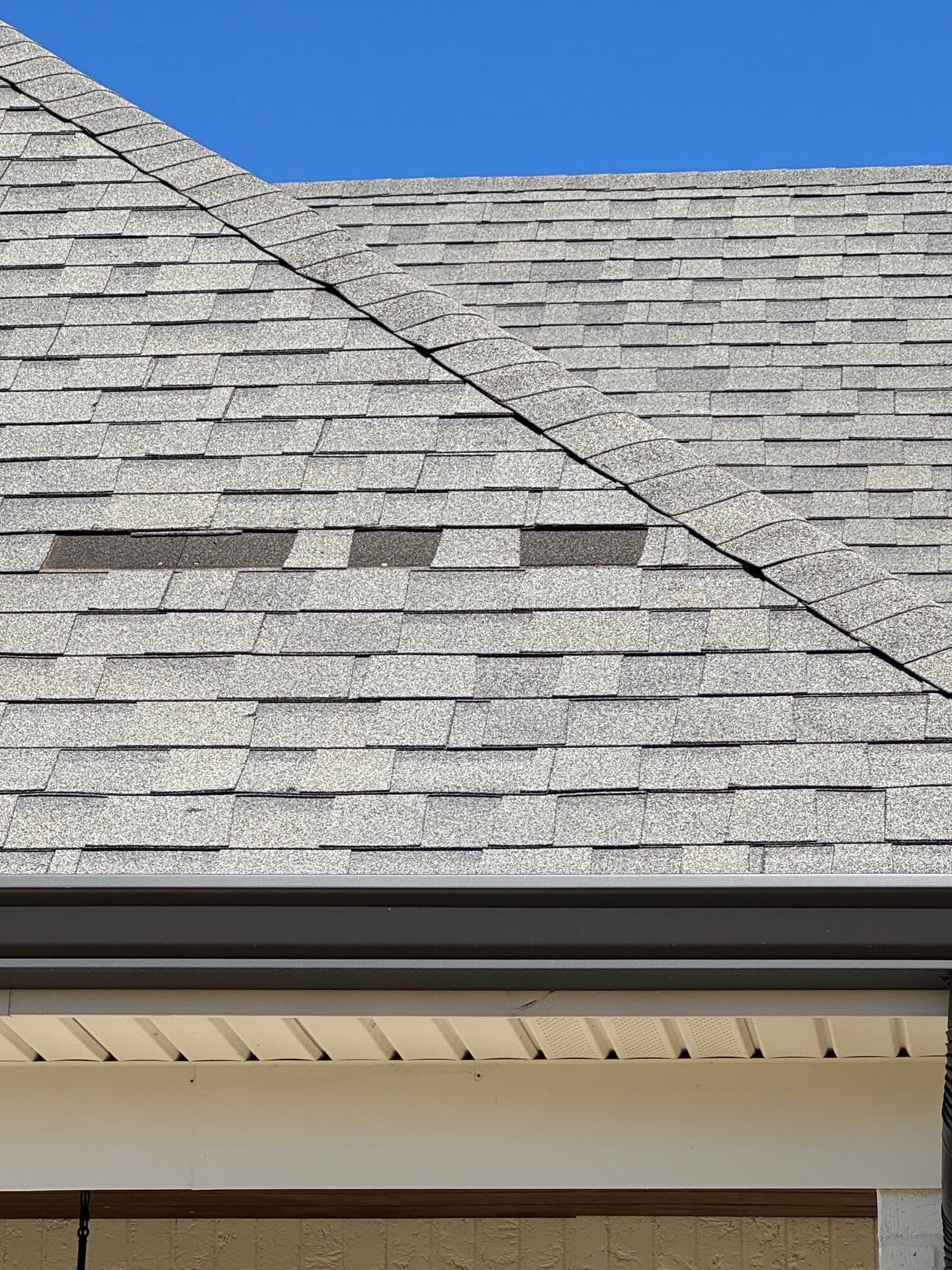 Shingle roof slope with wind-torn tabs missing above the soffit line