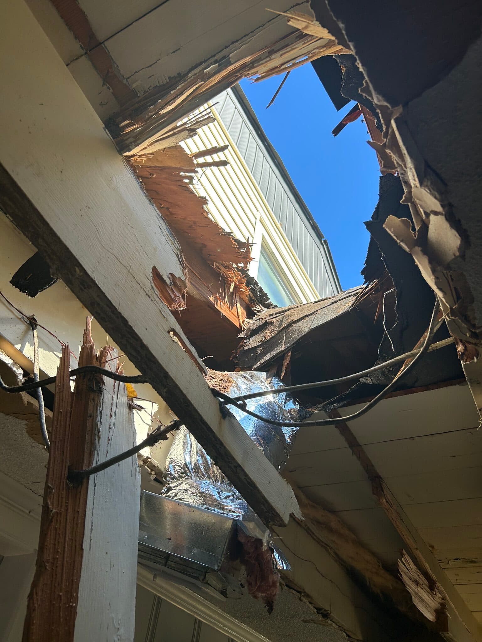 Hole punched through a roof overhang seen from below, with splintered framing and exposed ductwork