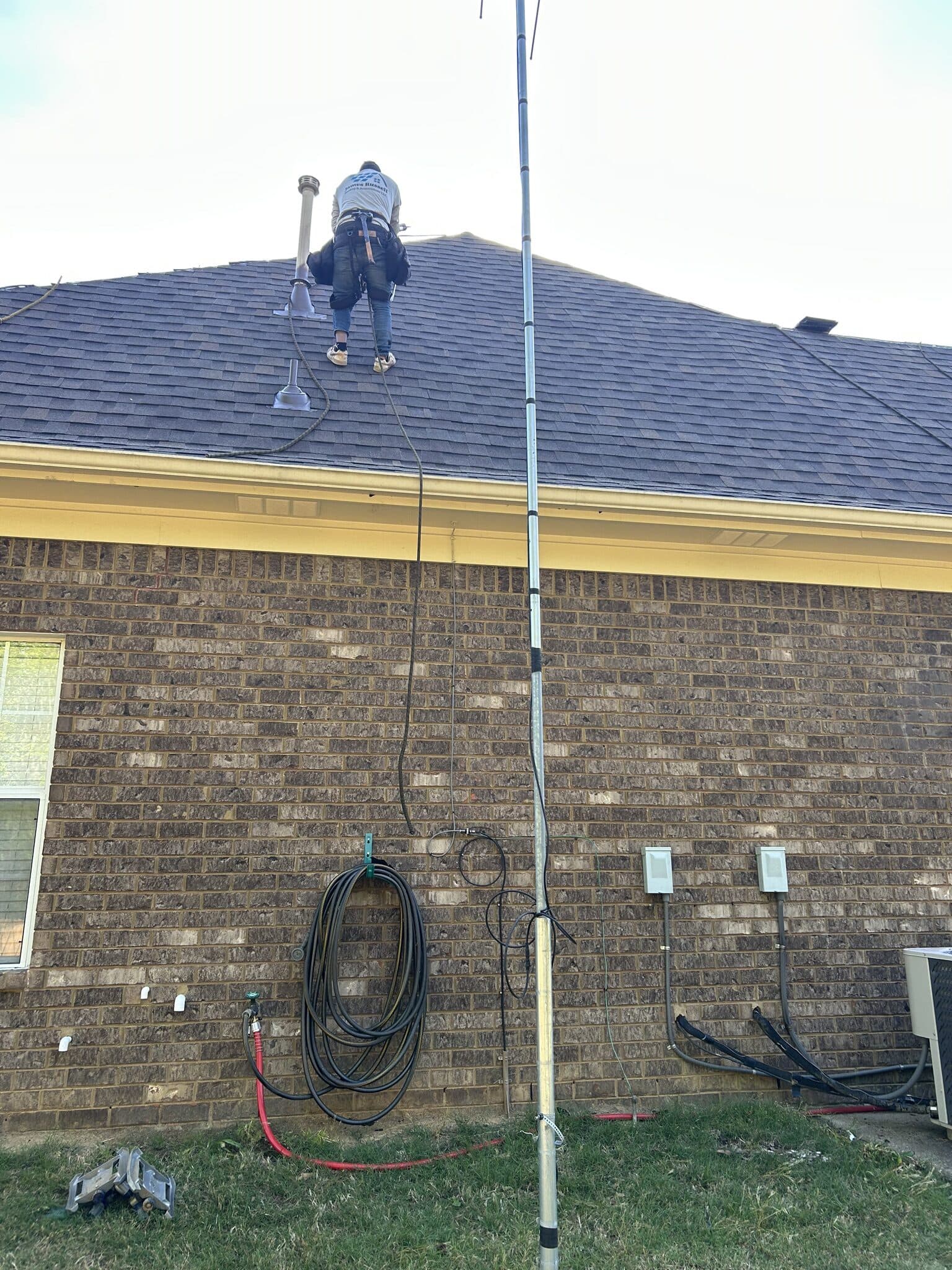 Crew member on a brick home's roof beside a tall mast