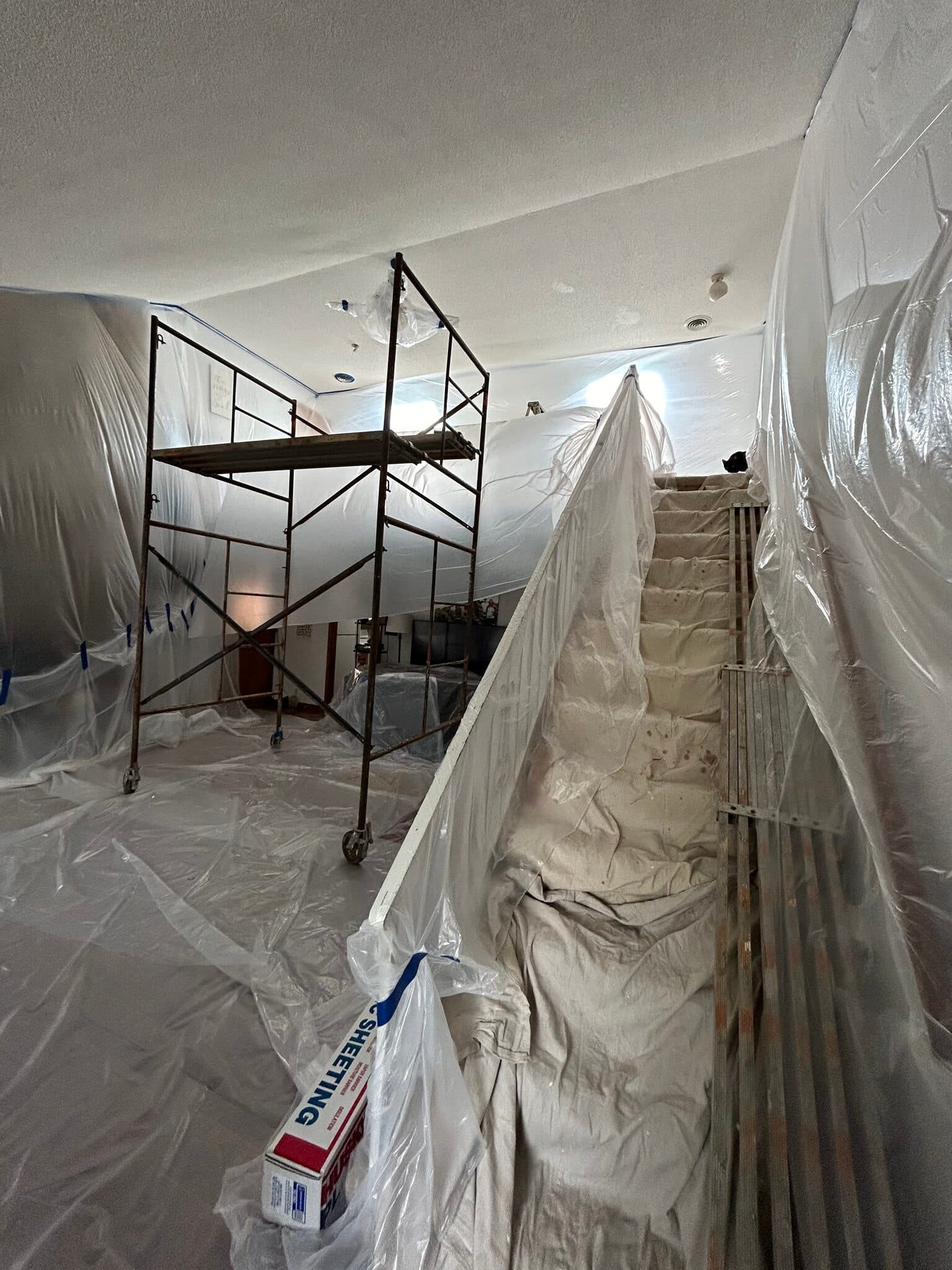 Scaffolding set up in a two-story room draped in plastic sheeting for ceiling drywall work