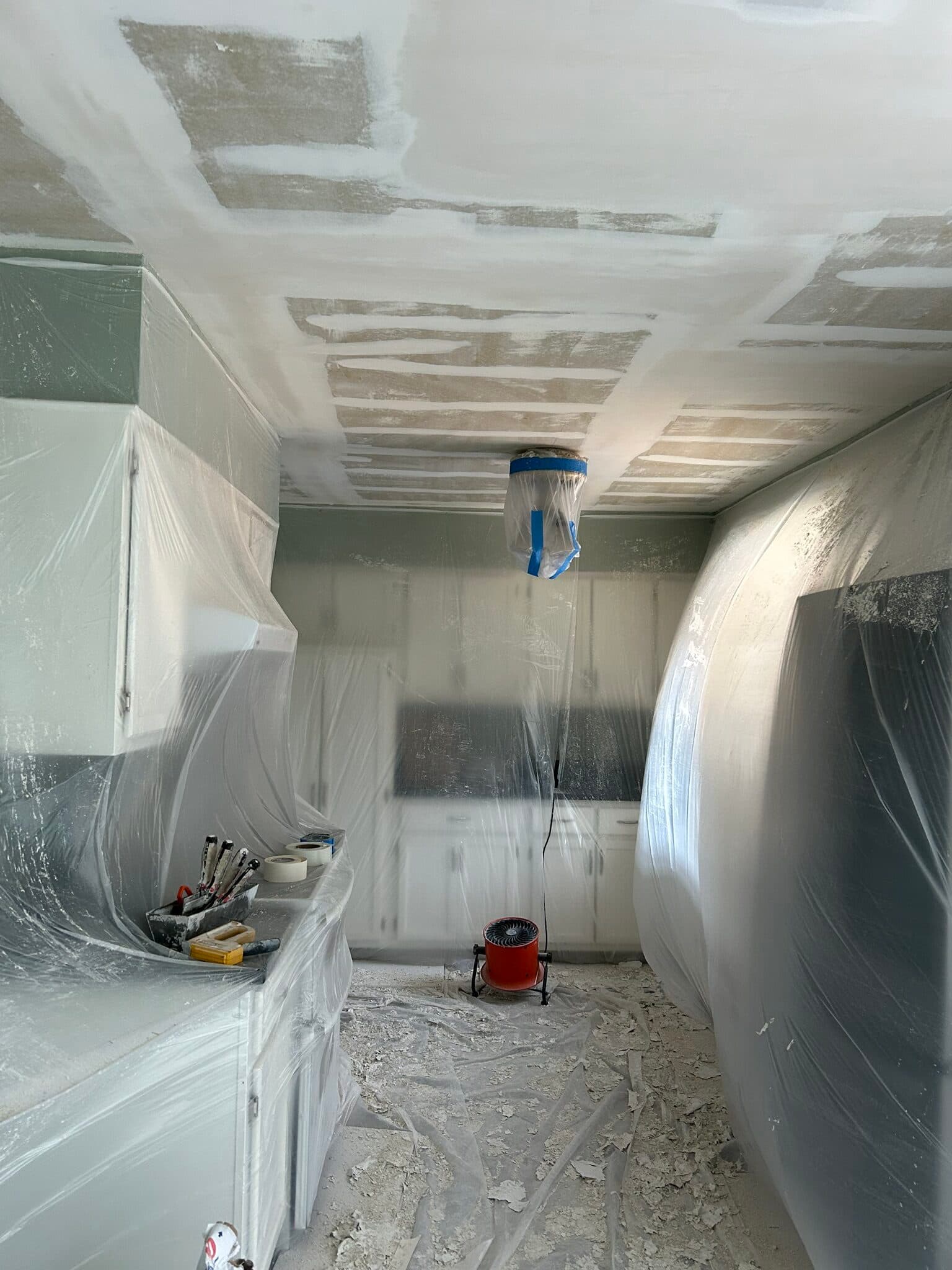 Kitchen ceiling repair in progress with mudded joints and plastic masking over the cabinets