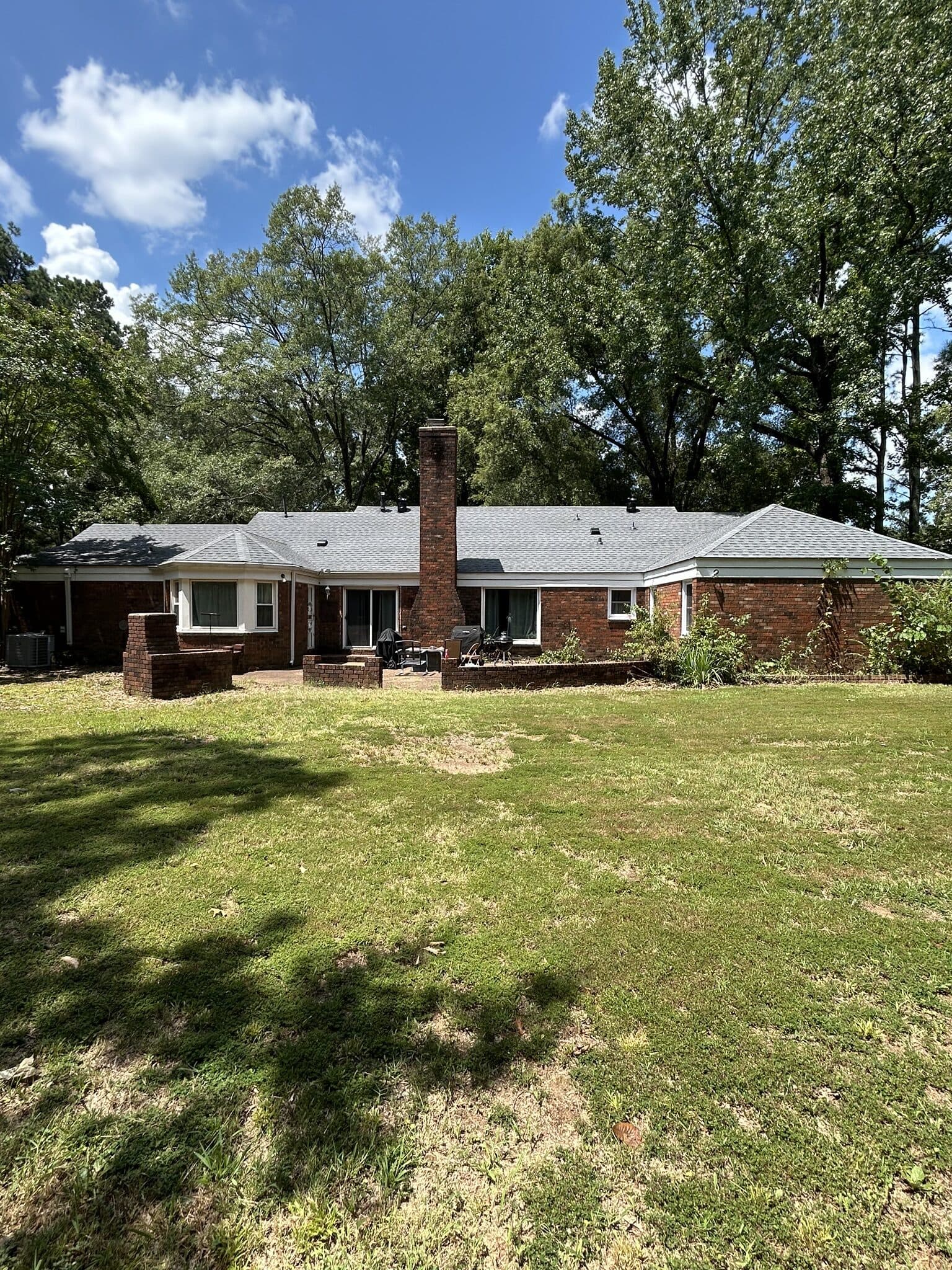 Brick ranch home and wide back lawn with a completed roof