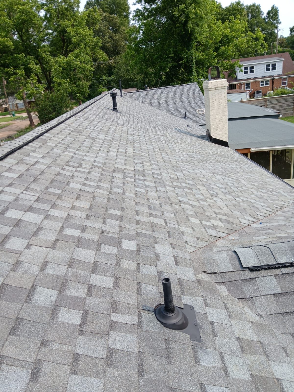 Wide field of light gray architectural shingles with a pipe boot and distant chimney