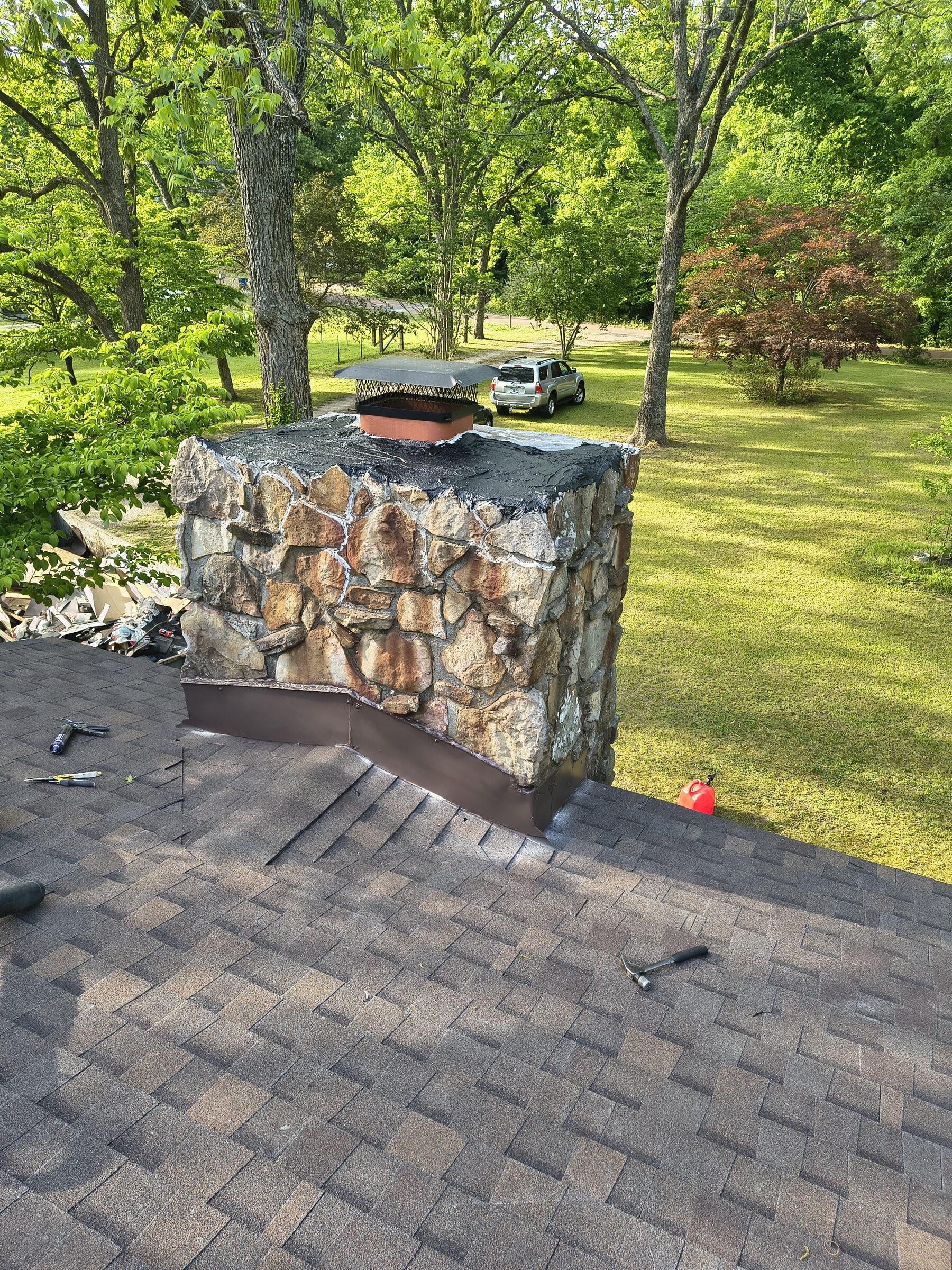 Stone chimney rising through a new shingle roof with a broad lawn behind
