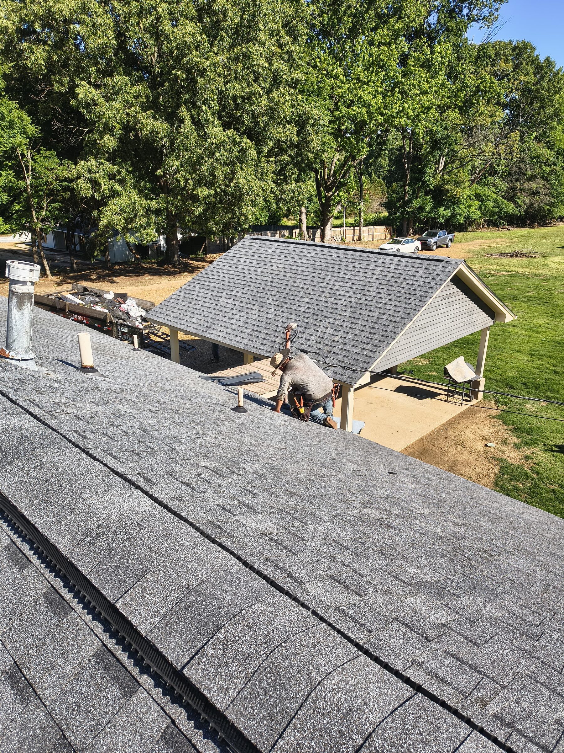View along a shingle ridge toward crew members working at the far end of the roof