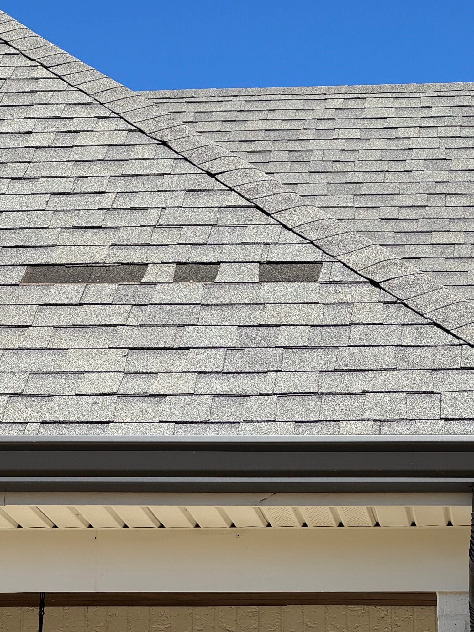 Shingle roof slope with wind-torn tabs missing above the soffit line