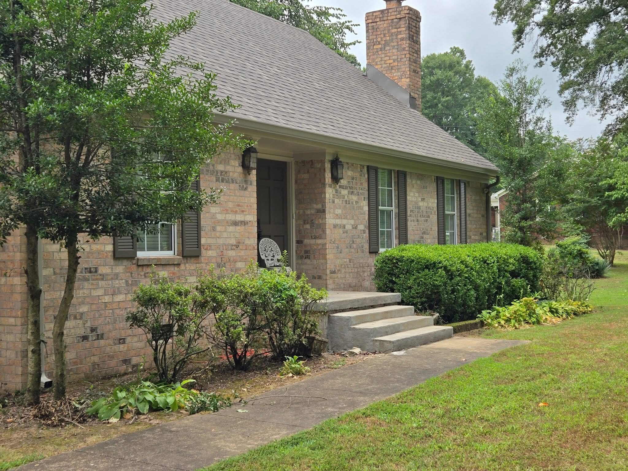 Brick ranch home with mature trees and a completed shingle roof
