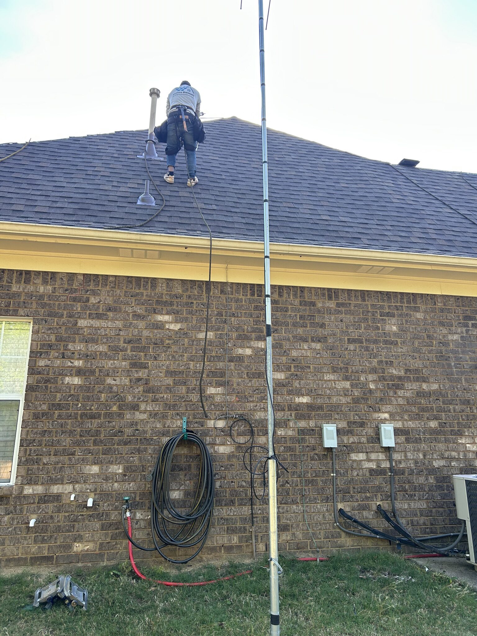 Crew member on a brick home's roof beside a tall mast