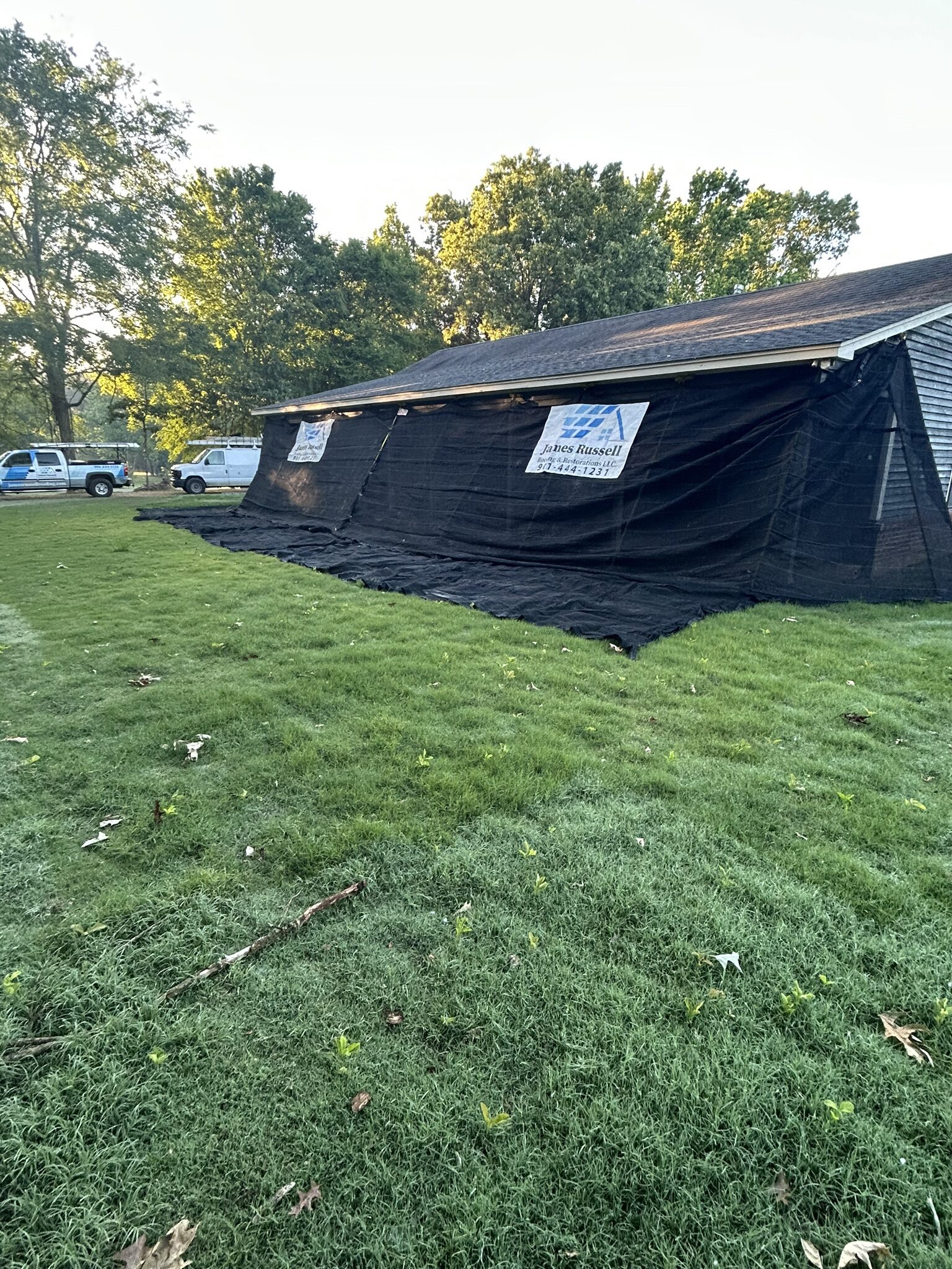 Home protected by black tarping across the roofline with a company sign on the lawn