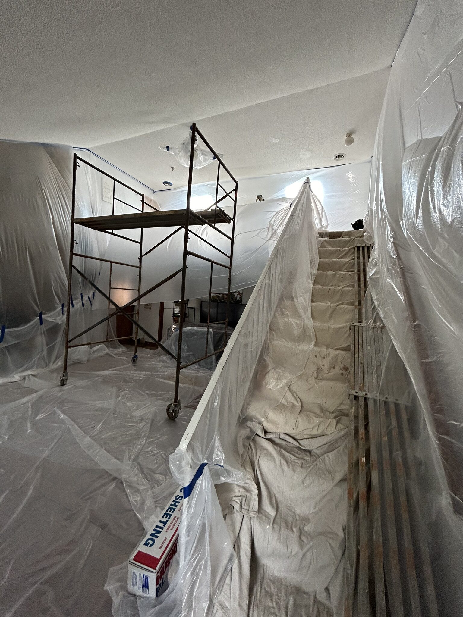 Scaffolding set up in a two-story room draped in plastic sheeting for ceiling drywall work