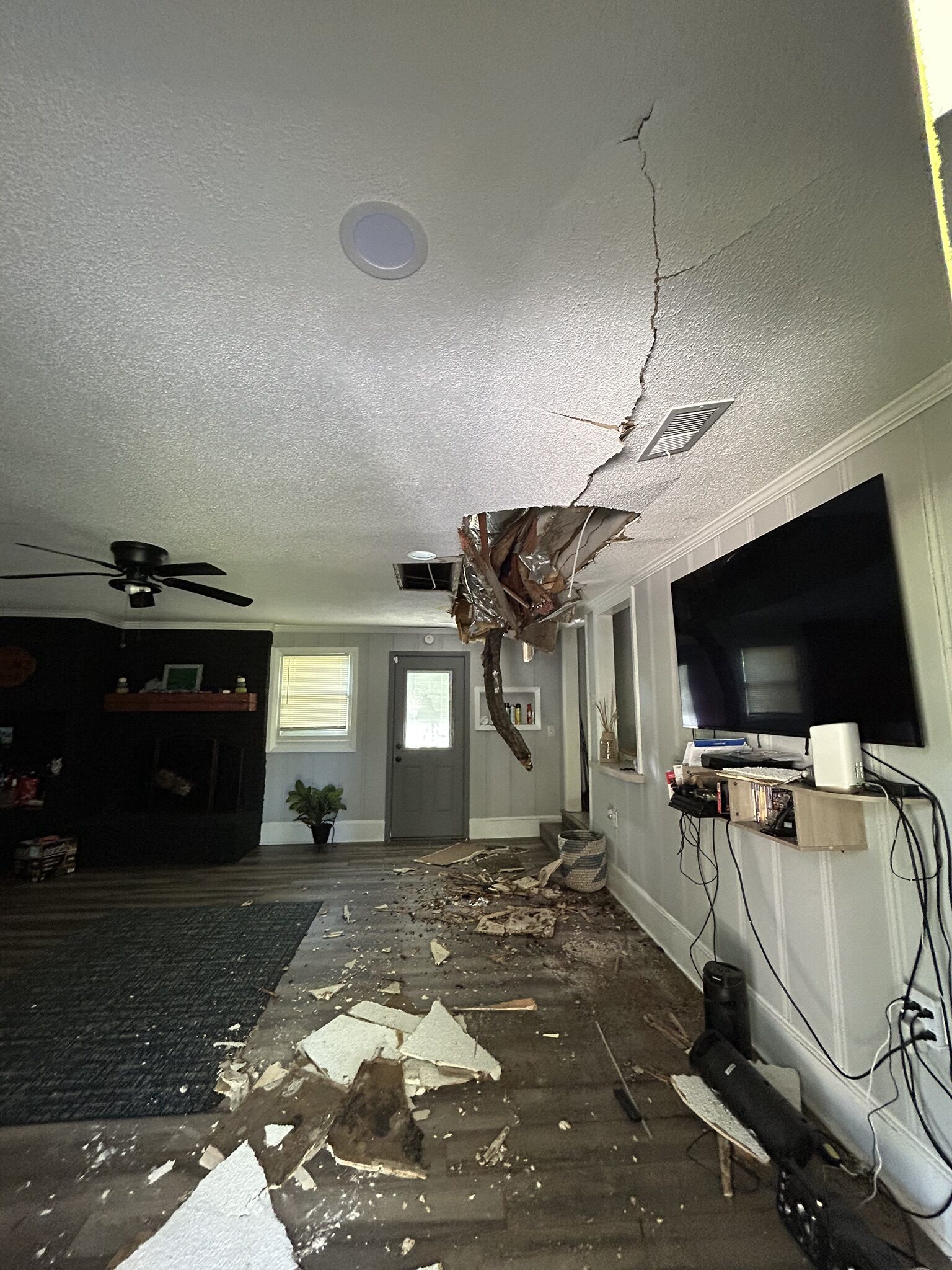 Living room ceiling broken open by a fallen limb with debris scattered across the floor